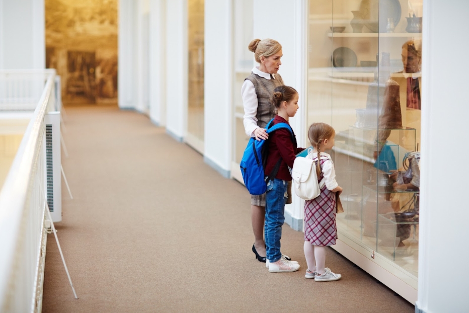 девочки с учителем смотрят на экспозицию через стекло из коридора школы